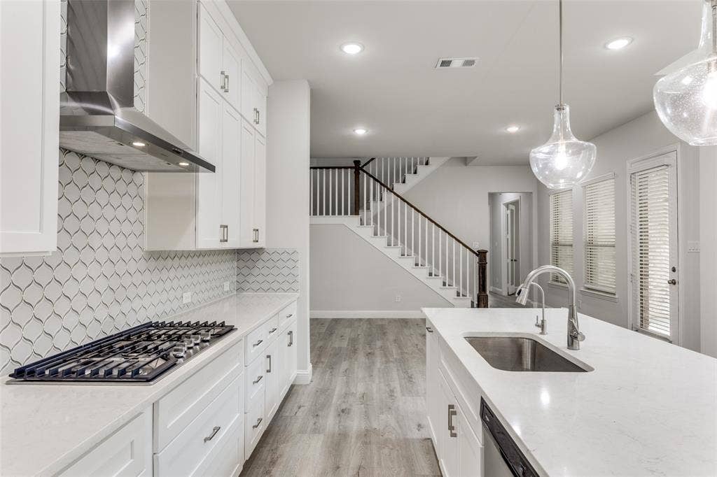 Kitchen featuring wall chimney range hood, a sink, stainless steel appliances, tasteful backsplash, and light wood finished floors