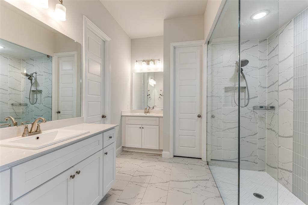 Bathroom featuring marble look tile flooring, a marble finish shower, two vanities, and recessed lighting