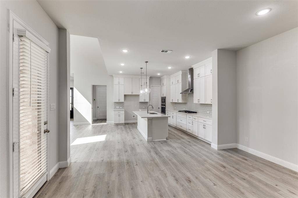 Kitchen featuring wall chimney range hood, light wood-type flooring, tasteful backsplash, white cabinetry, and light countertops