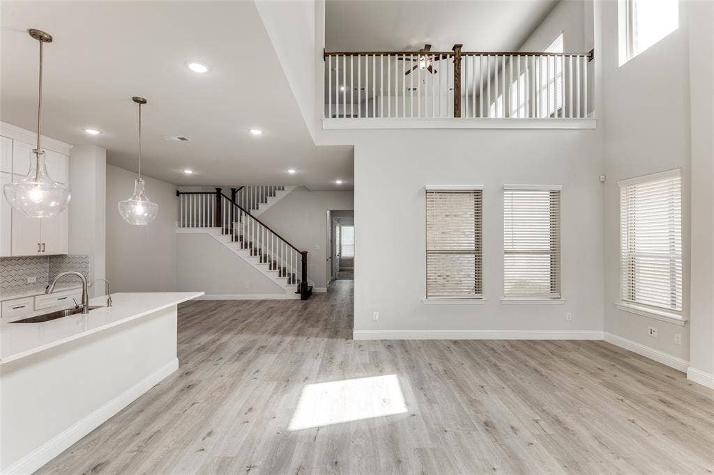Unfurnished living room featuring a sink, stairs, light wood finished floors, baseboards, and a high ceiling