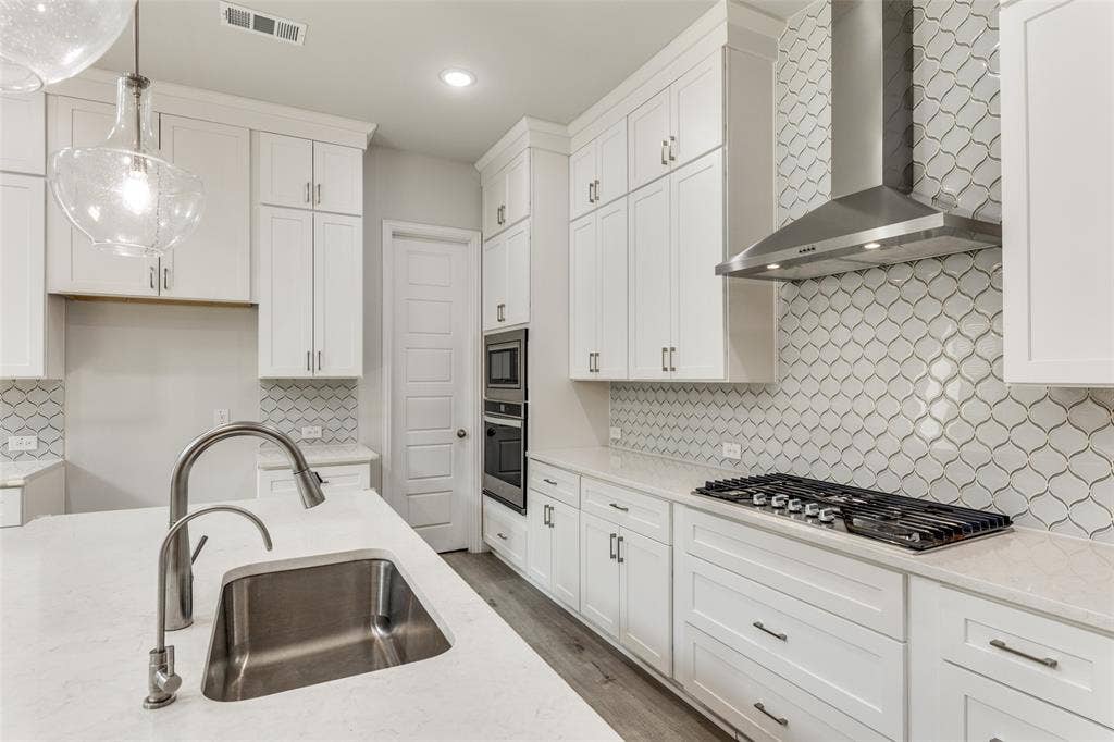 Kitchen featuring wall chimney range hood, appliances with stainless steel finishes, a sink, backsplash, and white cabinetry