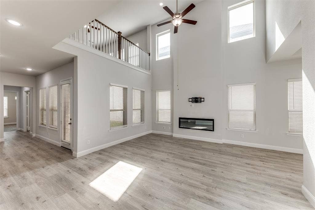Unfurnished living room with a towering ceiling, ceiling fan, baseboards, a glass covered fireplace, and light wood-type flooring