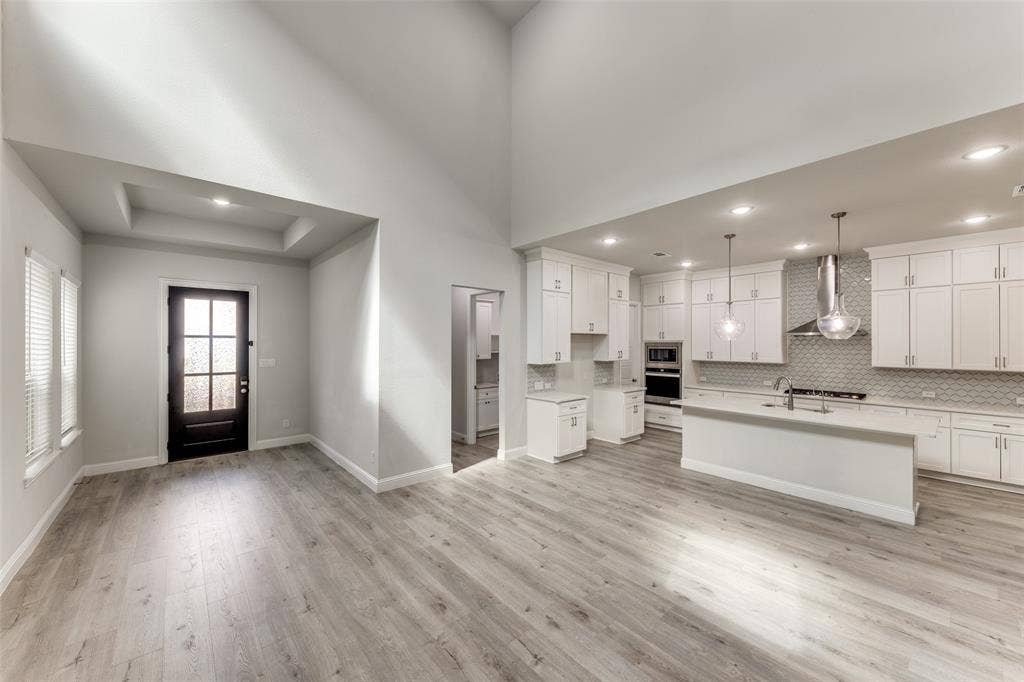 Kitchen with wall chimney range hood, stainless steel appliances, light countertops, light wood-style flooring, and recessed lighting