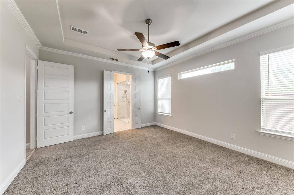 Unfurnished bedroom featuring a raised ceiling, carpet flooring, crown molding, baseboards, and connected bathroom