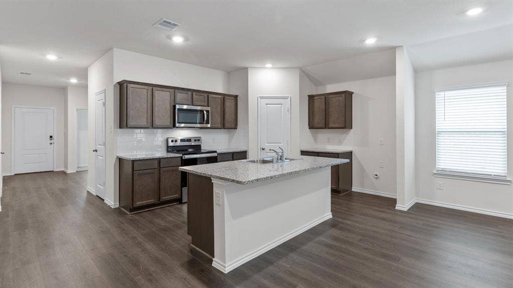 4028 Ripplewood Drive, Lindale, TX 75771 Kitchen featuring an island with a sink, stainless steel appliances, dark wood-finish cabinetry, and light-colored countertops