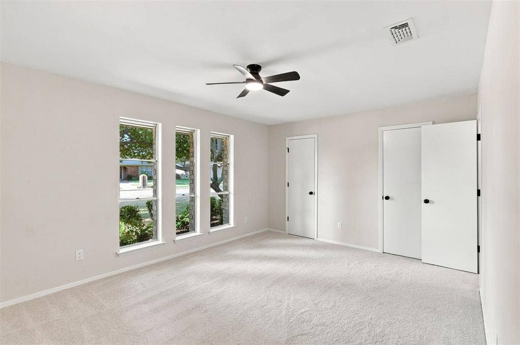Carpeted room featuring multiple windows, a ceiling fan with light fixture, and closet doors