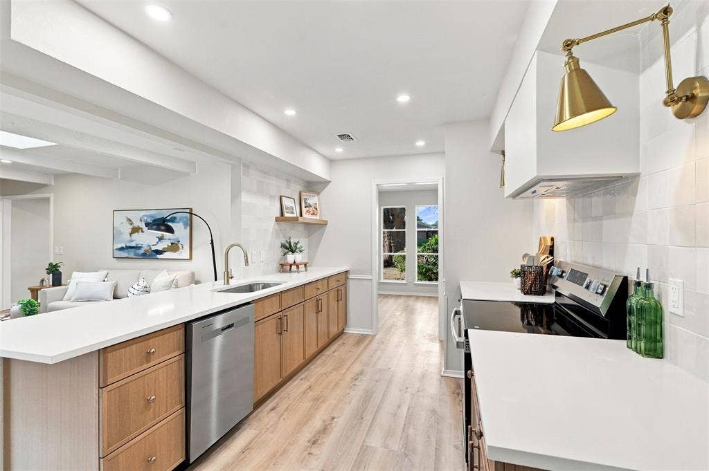 Contemporary kitchen featuring a stainless steel dishwasher, white countertops, wood-finish flooring, and recessed lighting