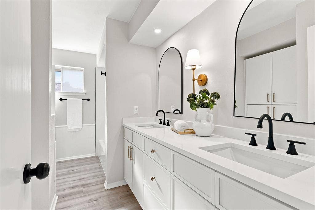 Dual vanity with integrated sinks, matte black fixtures, arched mirrors, built-in cabinetry, and wood-finish flooring