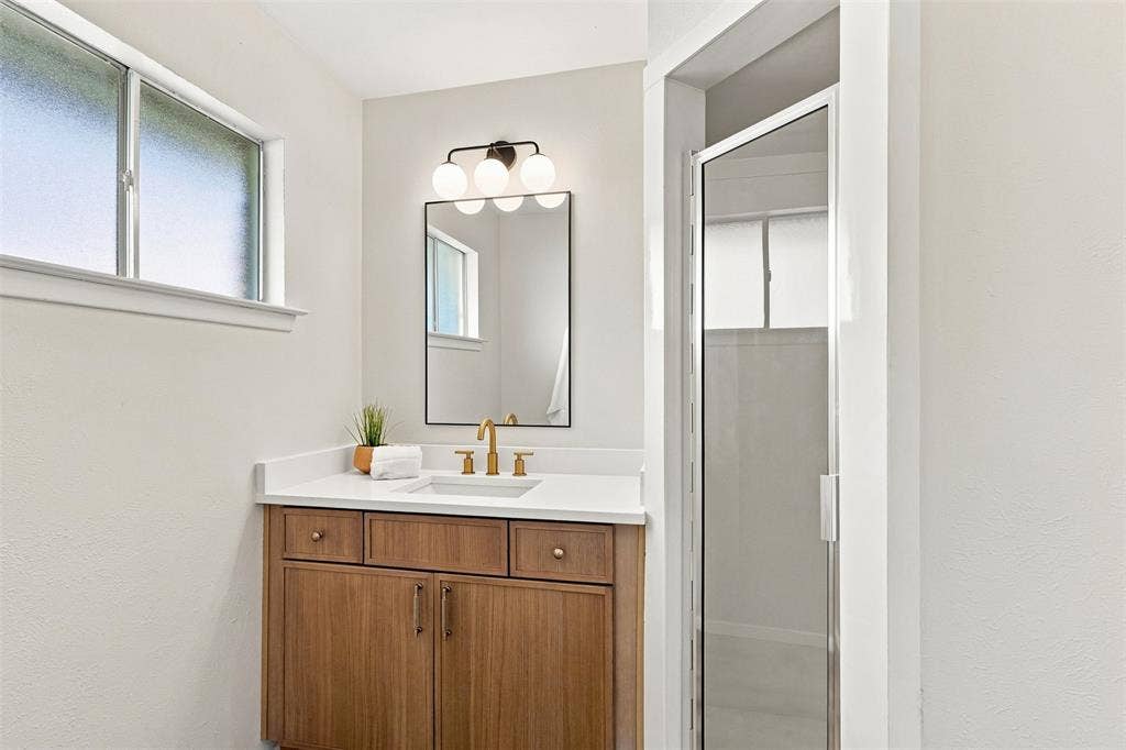 Wood-finish vanity with a white countertop and undermount sink, complemented by a rectangular mirror and a glass-enclosed shower
