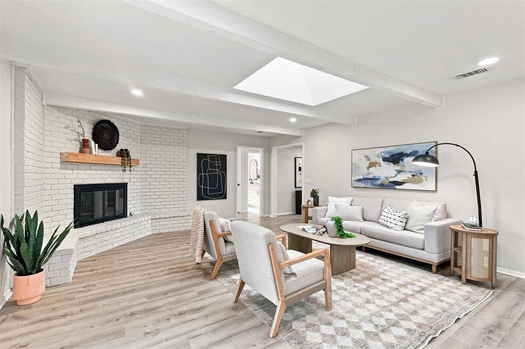 Wood-finish flooring throughout, white painted brick fireplace with wood mantel, skylight, recessed lighting, and exposed ceiling beams