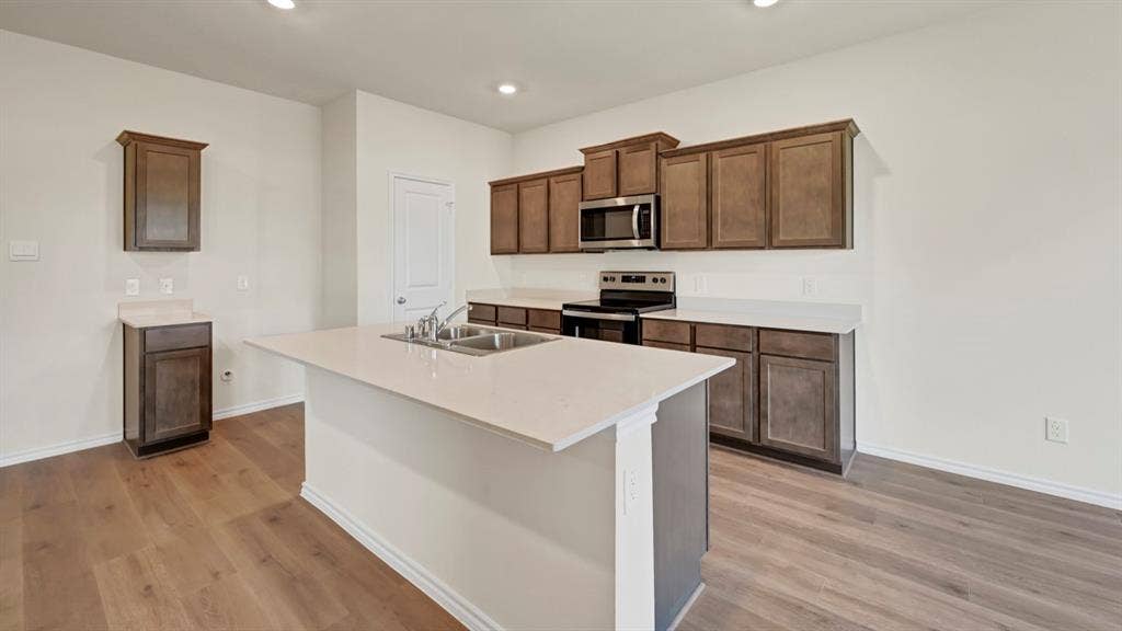 3058 Hidden Valley Drive, Lindale, TX 75771 Expansive kitchen island with an undermount double-basin sink, wood-finish flooring, dark wood cabinetry, and stainless steel appliances