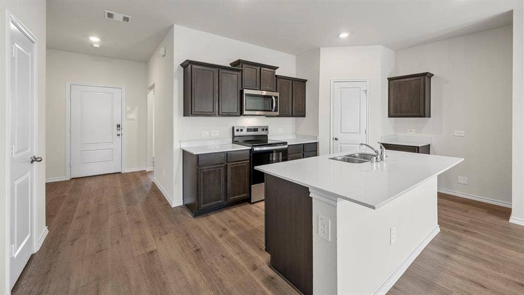 5028 Shumard Drive, Lindale, TX 75771 Modern kitchen featuring dark wood-finish cabinetry, stainless steel appliances, a center island with sink, white countertops, and wood-finish flooring
