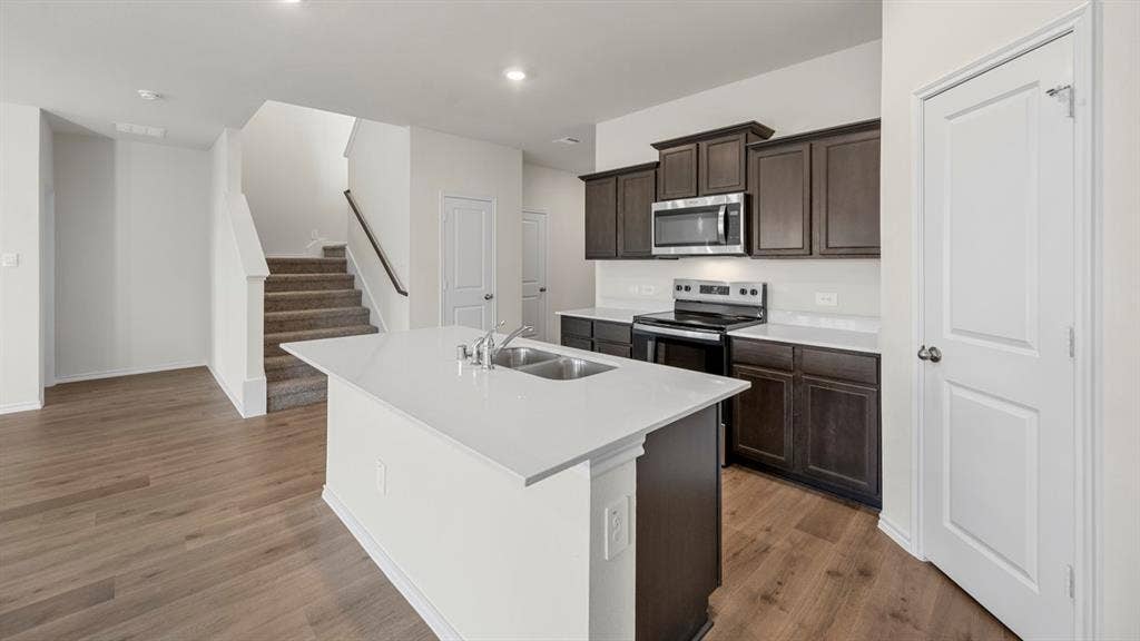 5028 Shumard Drive, Lindale, TX 75771 Modern kitchen with dark wood-finish cabinetry, stainless steel appliances, and a central island featuring a stainless steel double sink