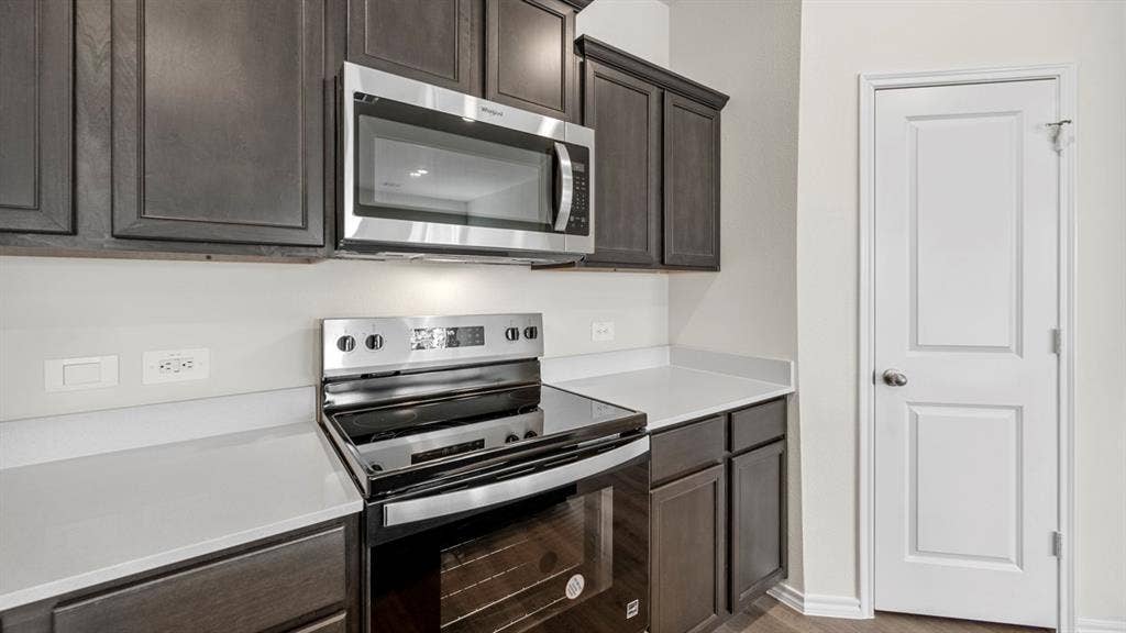 5028 Shumard Drive, Lindale, TX 75771 Dark wood-finish cabinetry with crown molding, stainless steel microwave, electric range, light-toned countertops, and a white paneled door
