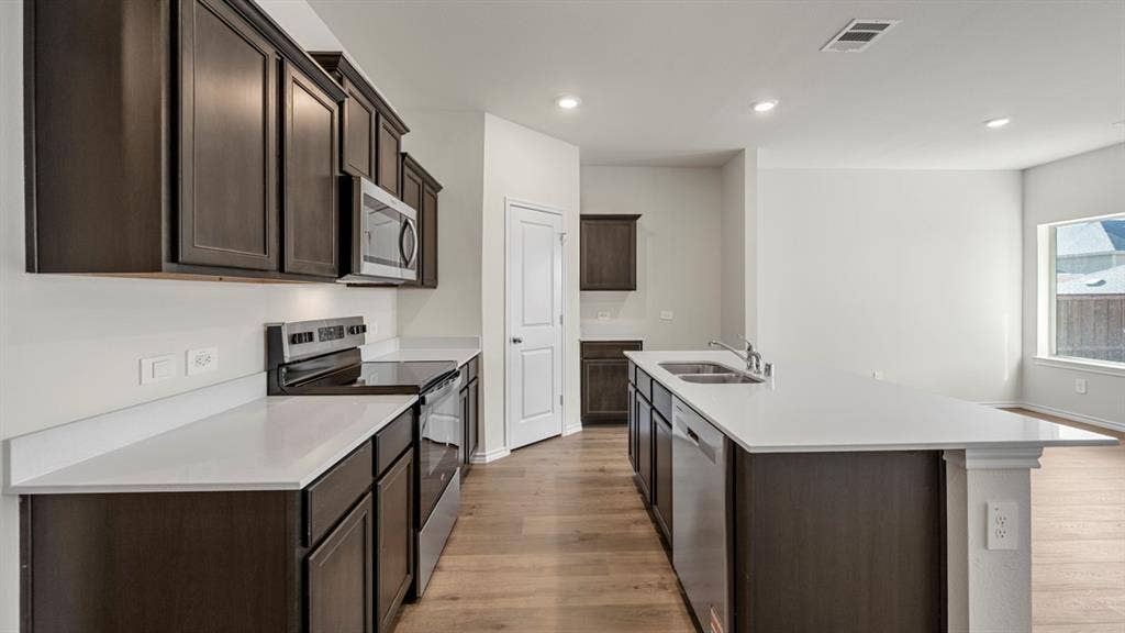 5028 Shumard Drive, Lindale, TX 75771 Kitchen featuring wood-finish flooring, dark wood cabinetry, white countertops, stainless steel appliances, and an island with an integrated sink