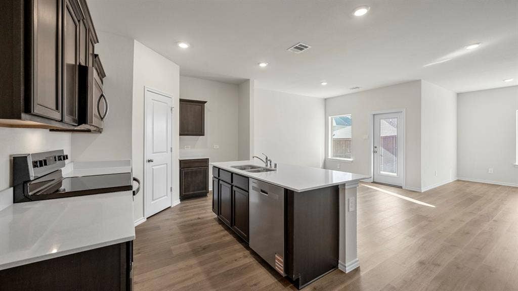 5028 Shumard Drive, Lindale, TX 75771 Kitchen featuring wood-finish flooring, dark wood-finish cabinetry, white countertops, and a kitchen island with a double basin sink