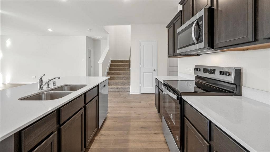 5028 Shumard Drive, Lindale, TX 75771 Kitchen featuring dark wood-finish cabinetry, light-toned countertops, stainless steel appliances, and a double basin sink with a chrome faucet