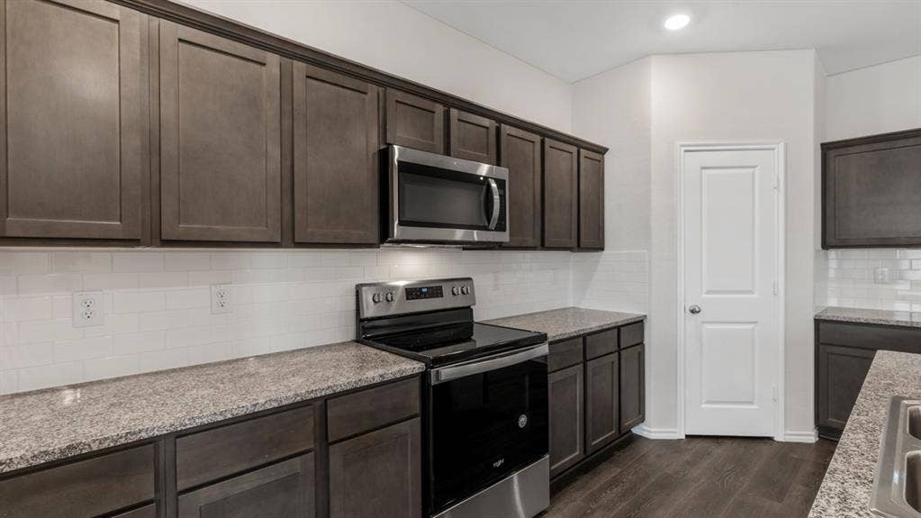 3037 Hidden Valley Drive, Lindale, TX 75771 Dark wood-finish cabinetry, light speckled countertops, stainless steel appliances, and white subway tile backsplash
