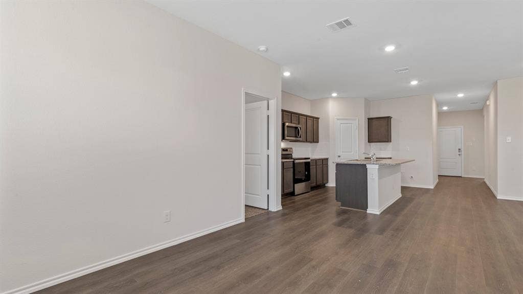 3037 Hidden Valley Drive, Lindale, TX 75771 Open-concept living area with dark wood-finish flooring, recessed lighting, and a kitchen featuring dark cabinetry, stainless steel appliances, and a breakfast bar island