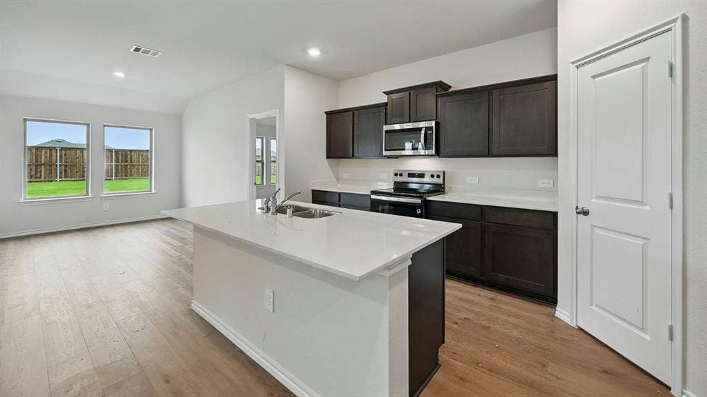 181 Brooks Street, Bullard, TX 75757 Kitchen featuring an island with a double basin sink, dark wood-finish cabinetry, stainless steel appliances, and a light-toned countertop