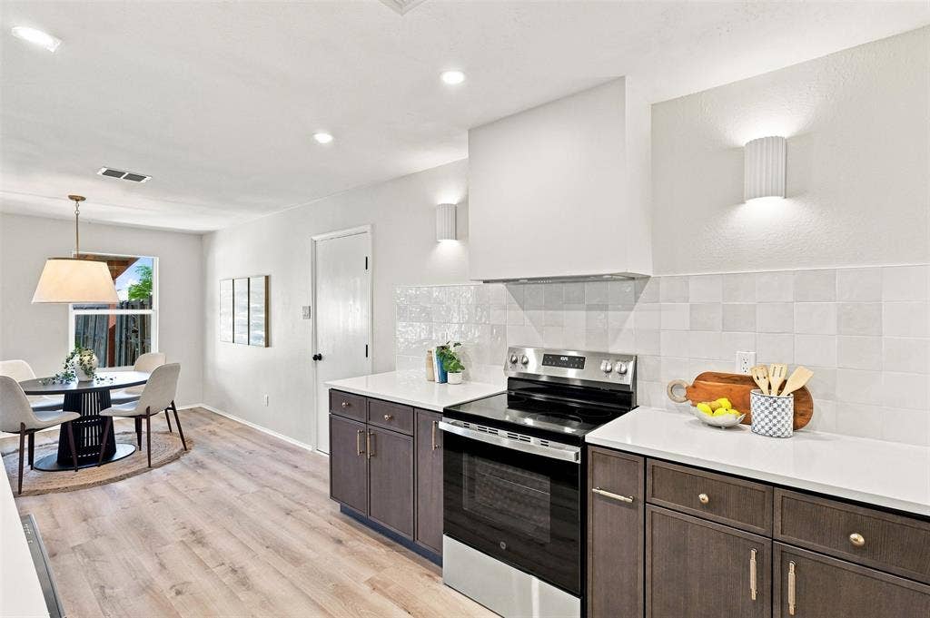1406 Quail Meadow Drive, Wylie, TX 75098 Stainless steel range with a custom range hood, white tile backsplash, light wood-finish flooring, and dark wood cabinetry with contrasting hardware