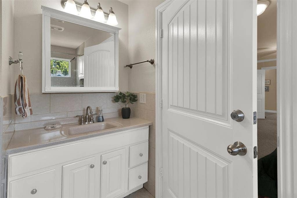2720 Oates Drive, Mesquite, TX 75150 White vanity with an integrated sink and brushed nickel faucet, framed mirror with overhead lighting, and beadboard interior door