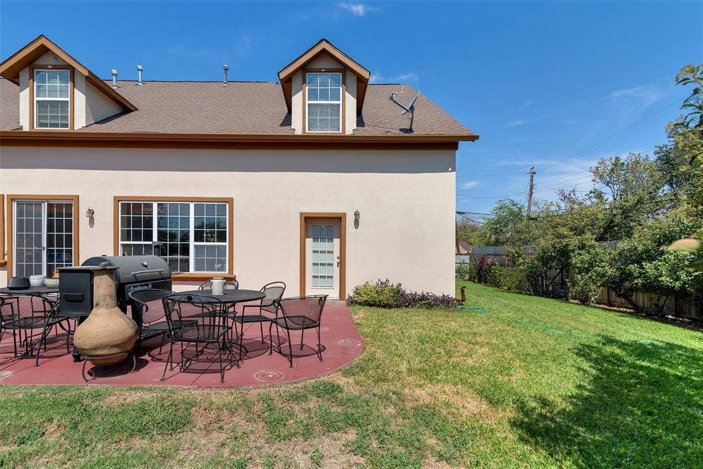 2720 Oates Drive, Mesquite, TX 75150 Expansive backyard featuring a red concrete patio, sliding glass door access, multiple windows, a side entry door, and dormer windows on the second level