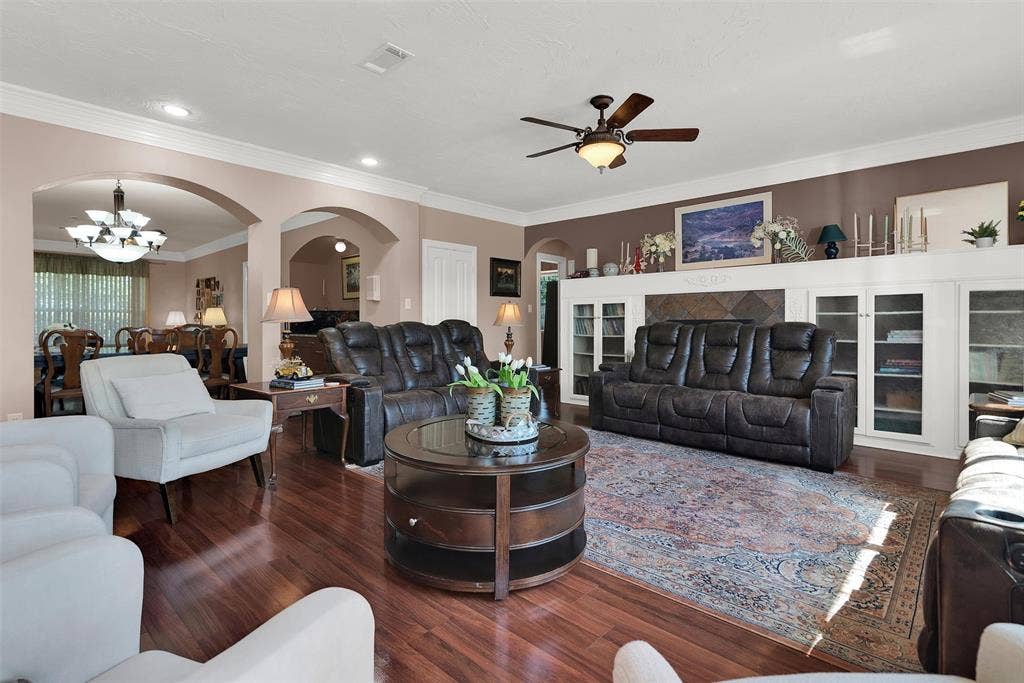2720 Oates Drive, Mesquite, TX 75150 Hardwood-finish flooring throughout, tray ceiling with a built-in fan, custom built-in cabinetry with glass-front doors, decorative archways, and crown molding