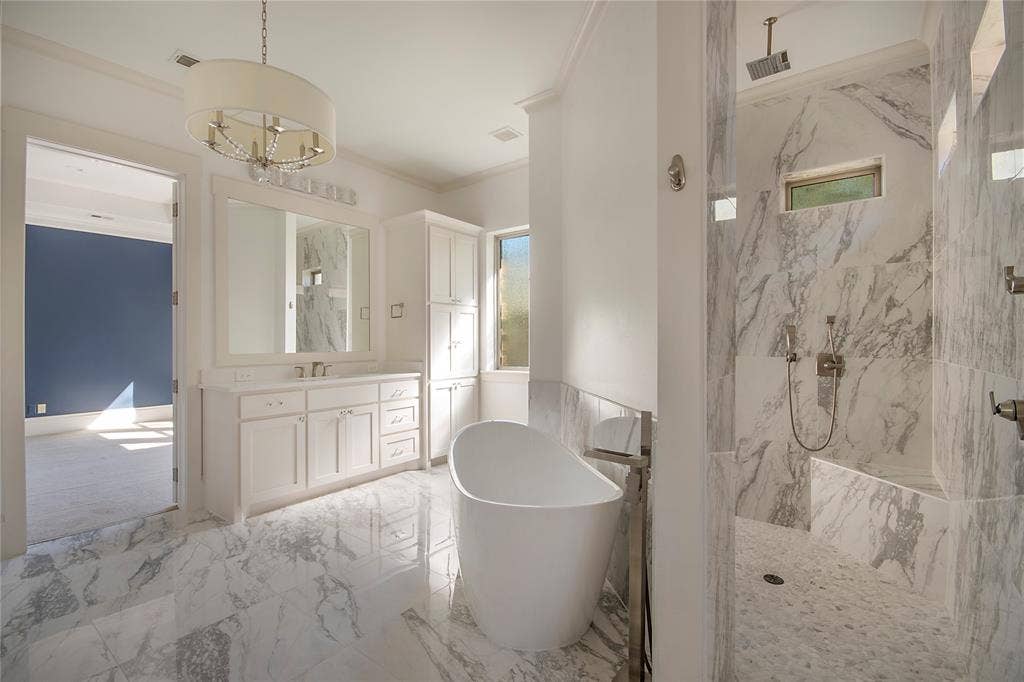 Spacious bathroom featuring a freestanding tub, a walk-in shower with a built-in bench, a double vanity, and marble-look tile flooring