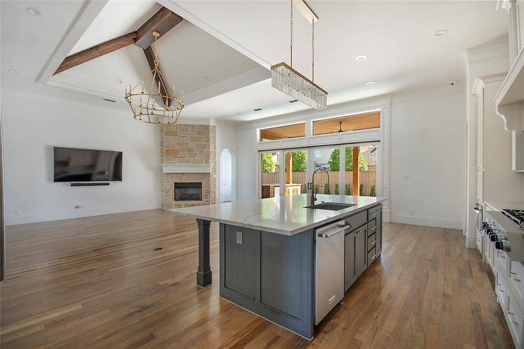Open-concept area featuring hardwood flooring, a stone fireplace, and a kitchen island with a built-in sink and dishwasher