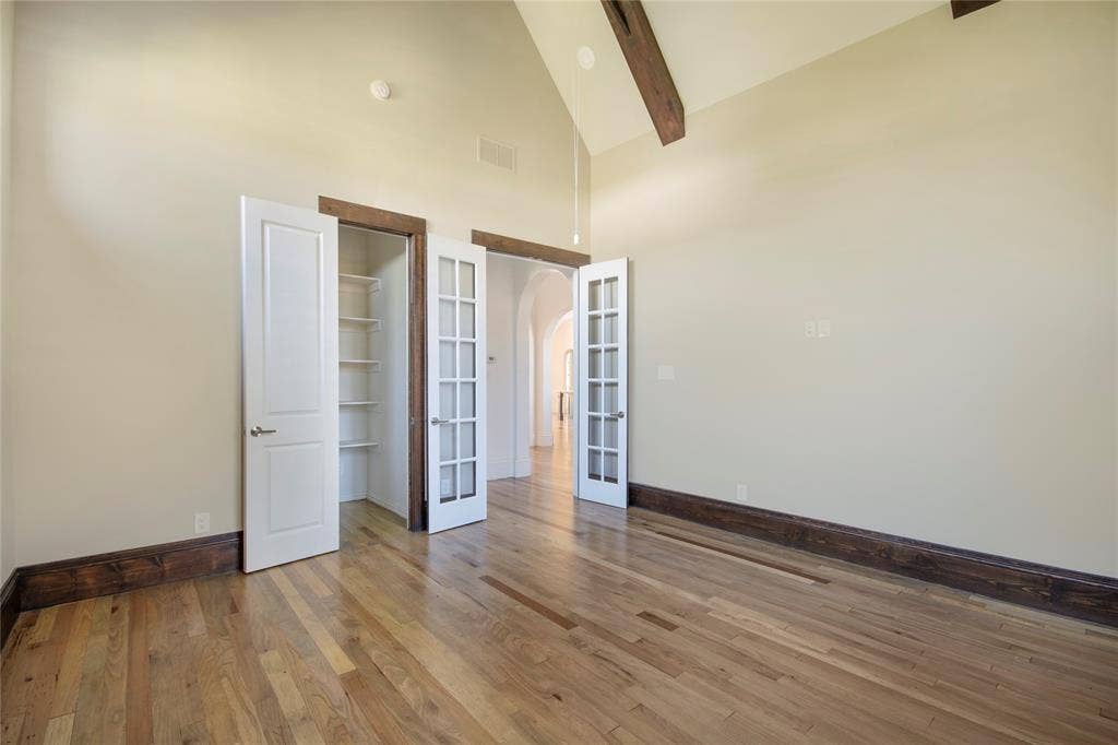 Vaulted ceiling with exposed wood beams, wood-finish flooring, white panel door, white French doors, and built-in shelving