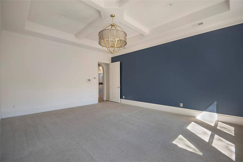 Coffer ceiling with recessed lighting, decorative chandelier, dark accent wall, carpeted flooring, and an arched doorway