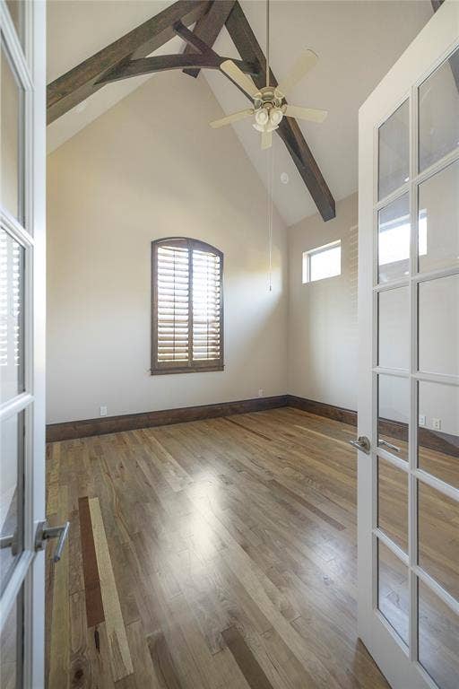 Vaulted ceiling with exposed wood beams, wood-finish flooring, and a ceiling fan with light fixture