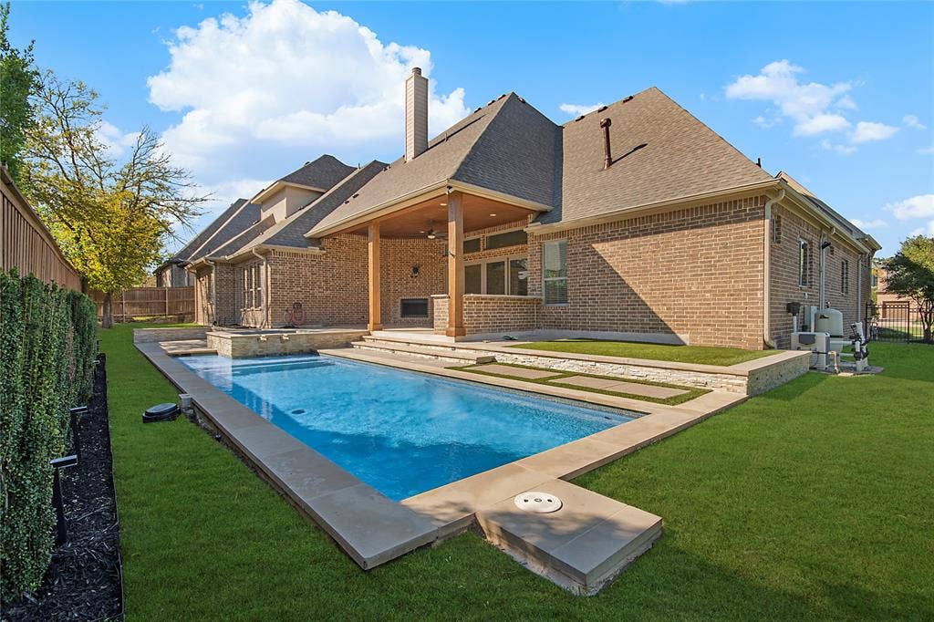 Brick exterior with a covered patio, outdoor fireplace, and a rectangular swimming pool