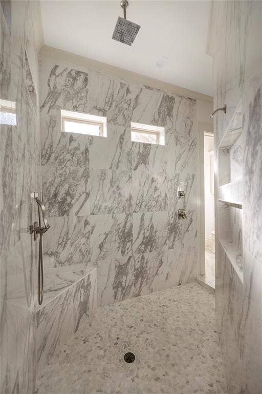 Walk-in shower featuring large format wall tiling, pebble-finish flooring, a built-in bench, a rain showerhead, and a handheld shower fixture