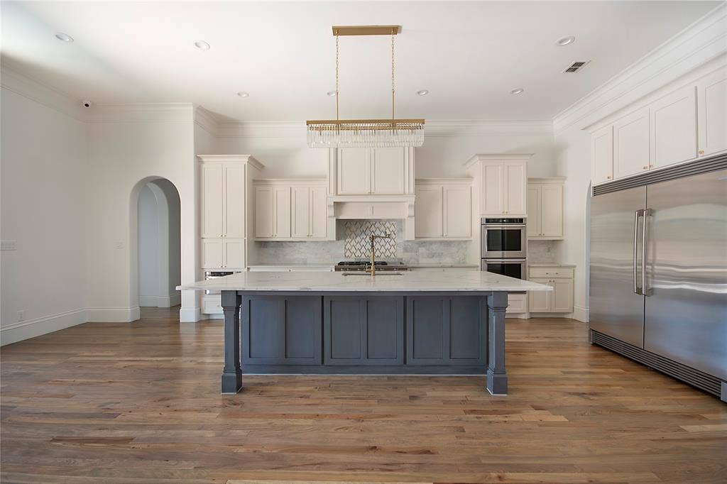 Gourmet kitchen featuring a large central island with seating, stainless steel double ovens, a built-in refrigerator, and wood-finish flooring
