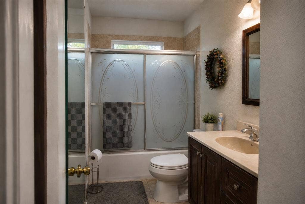 5012 Wateka Drive, Dallas, TX 75209 Spa-inspired bathroom featuring a frameless glass-enclosed shower with decorative tile accents, dual vanity with wood-finish cabinetry and white countertop, and brushed nickel fixtures