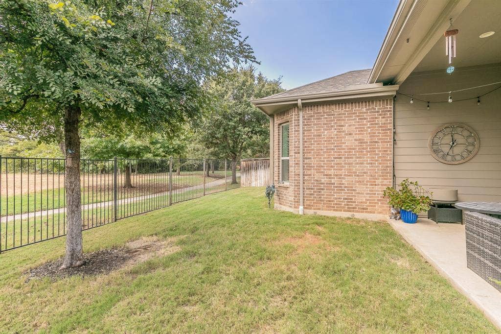 313 Elkhorn Trail, Keller, TX 76248 Brick exterior with a covered patio, string lighting, and an adjacent grassy area with mature trees and a black metal fence