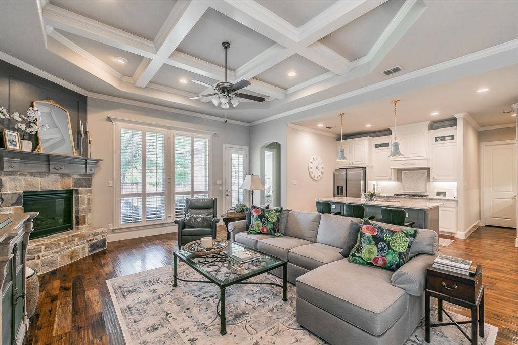 313 Elkhorn Trail, Keller, TX 76248 Coffered ceilings, stone-clad fireplace with mantel, wood flooring, plantation shutters, and a kitchen featuring white cabinetry and a central island with pendant lighting