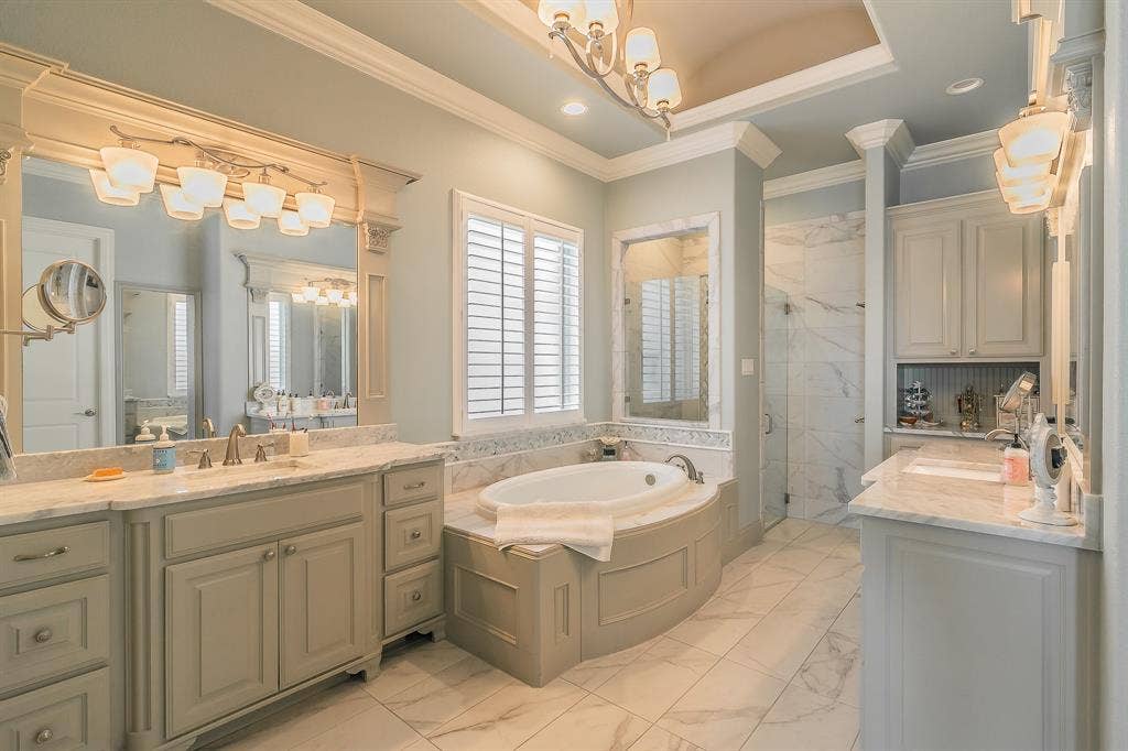 313 Elkhorn Trail, Keller, TX 76248 Spa-inspired primary bathroom featuring dual vanities with marble-finish countertops, an oversized soaking tub with built-in surround, a walk-in shower with glass enclosure, coffered ceiling detail, and recessed lighting throughout