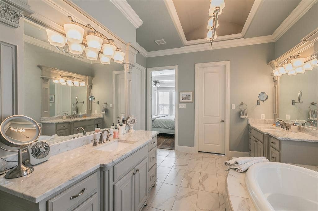 313 Elkhorn Trail, Keller, TX 76248 Dual vanities with beautiful countertops, tiled flooring, an oval soaking tub, and a decorative tray ceiling with an overhead light fixture