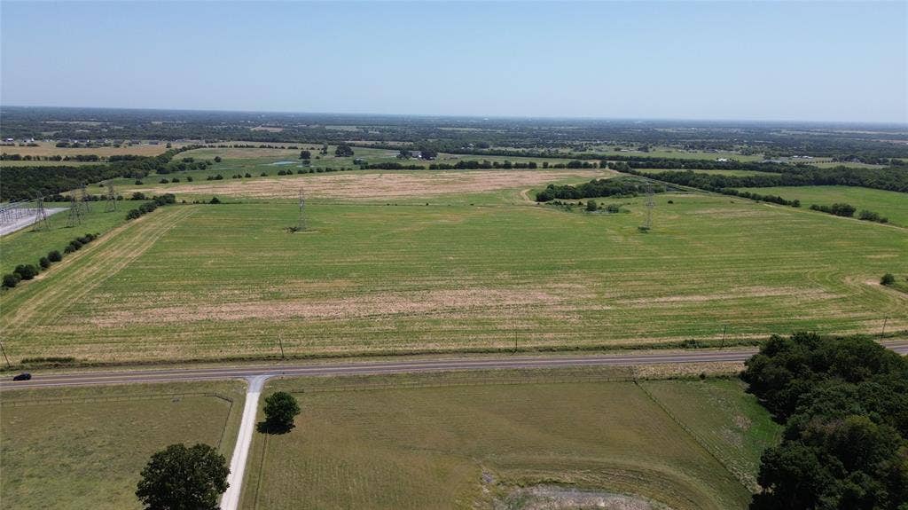 1566 Fm 2194, Farmersville, TX 75442 Expansive land parcel with clear skies, featuring a paved road, scattered trees, and visible power lines