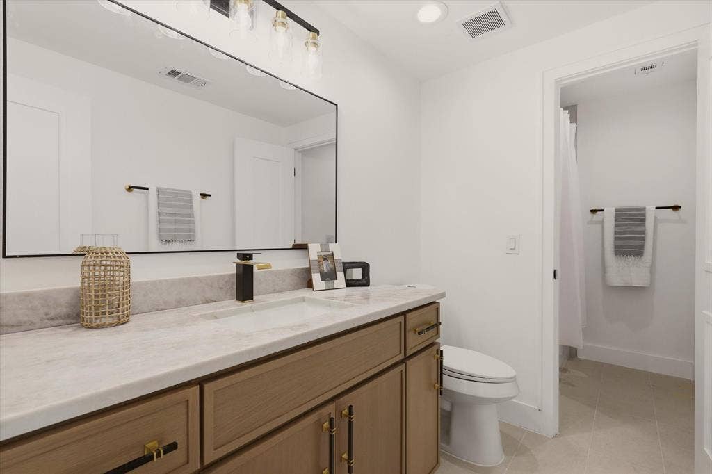 Light-finish wood vanity with gold hardware, a rectangular undermount sink, and a stone-finish countertop