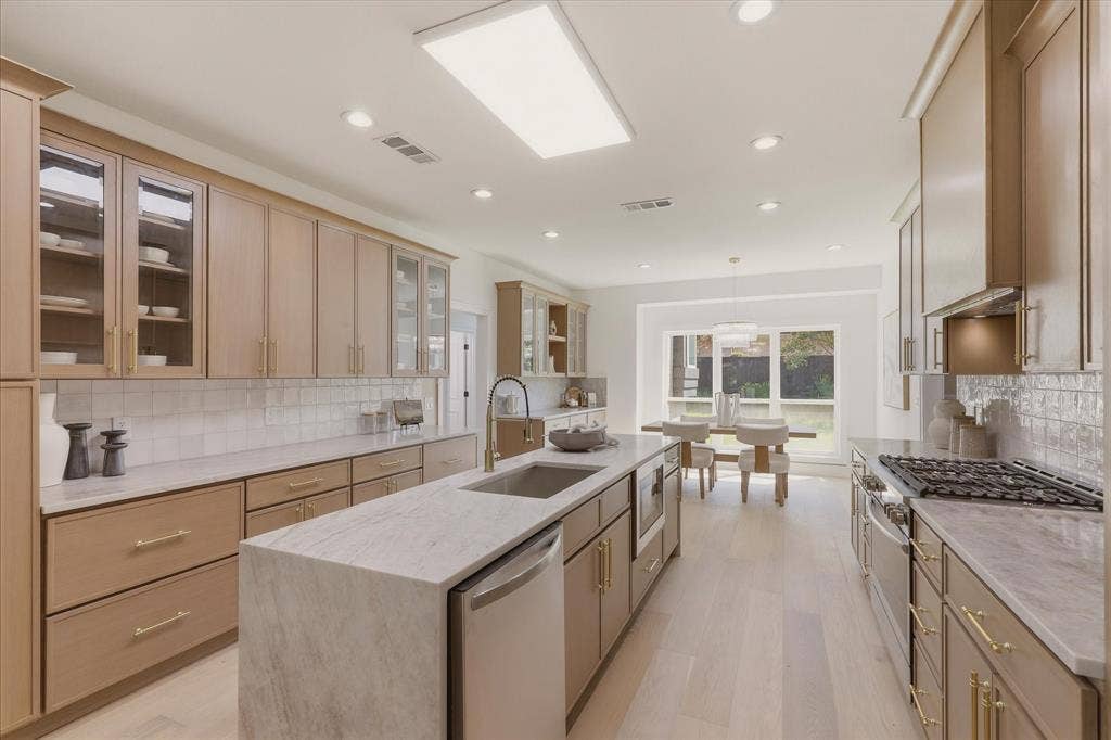 Gourmet kitchen with light wood-finish cabinetry, stone countertops, stainless steel appliances, and a central island with an undermount sink
