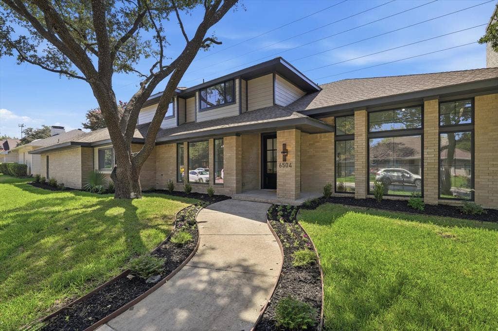 Brick facade, large windows, landscaped beds, mature tree, curved walkway