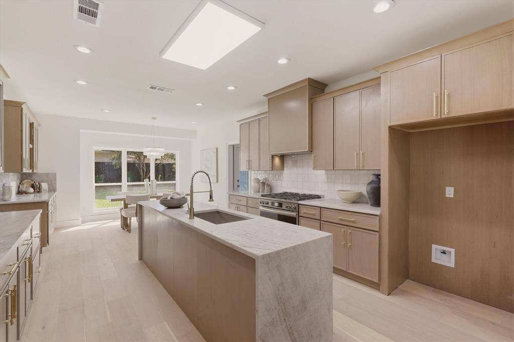 Integrated kitchen with a central island featuring a sink and faucet, light wood-finish cabinetry, subway tile backsplash, and light wood-finish flooring