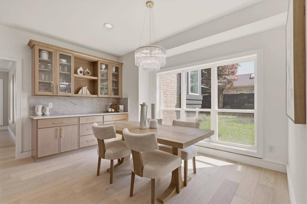 Light wood-finish flooring, built-in cabinetry with glass display doors, large picture window, recessed lighting, and a tiered chandelier