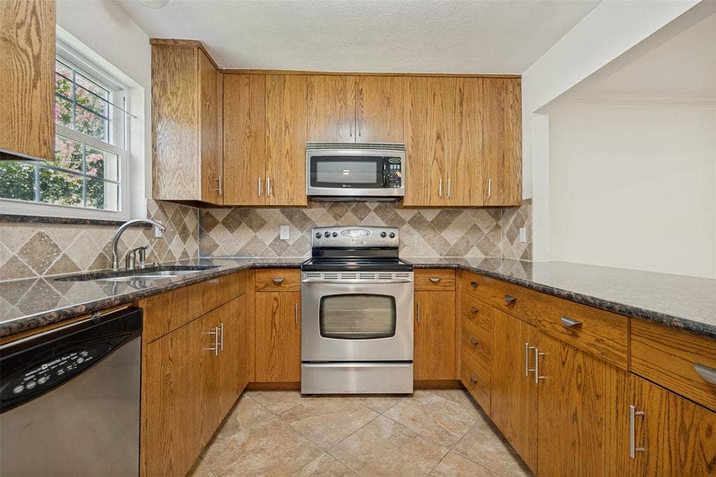 5818 E University Boulevard, #138, Dallas, TX 75206 U-shaped kitchen featuring wood-finish cabinetry, stainless steel appliances, and a tiled backsplash