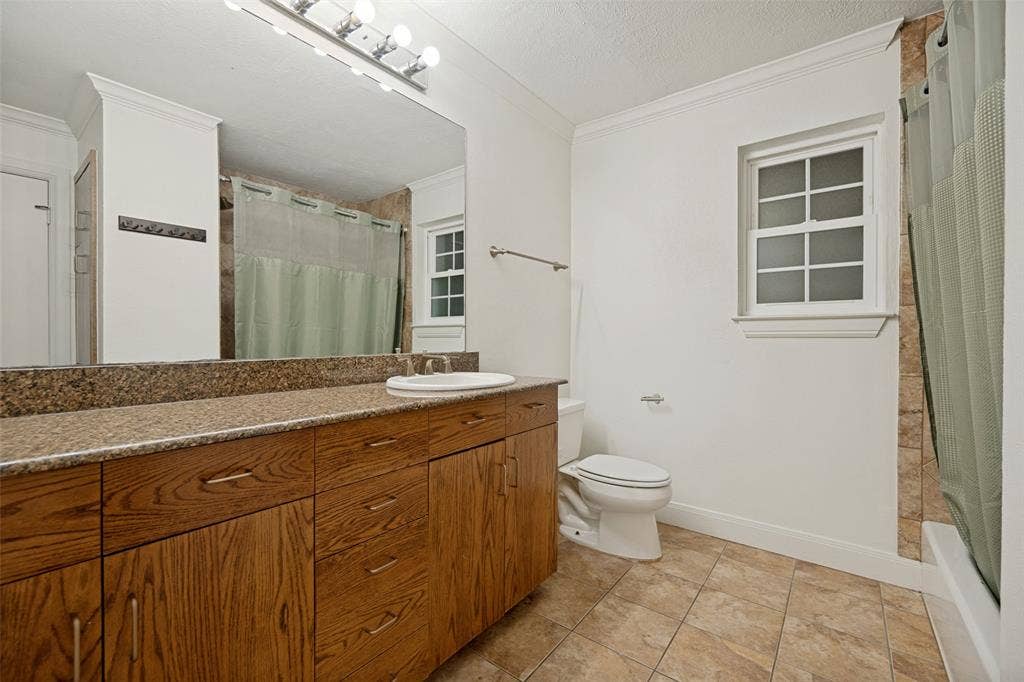 5818 E University Boulevard, #138, Dallas, TX 75206 Wood-finish vanity with an integrated sink, granite-style countertop, large wall-mounted mirror, ceramic tile flooring, and a window providing natural illumination