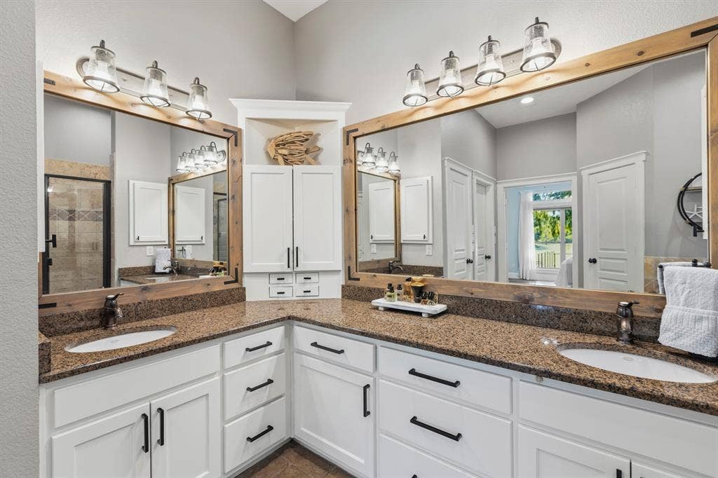 6810 Trinity Falls Parkway, McKinney, TX 75071 Dual vanity with stone countertops, white cabinetry, dark hardware, and large wood-framed mirrors